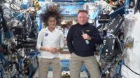 a woman in a white shirt and a man in a blue shirt stand inside a crowded space module
